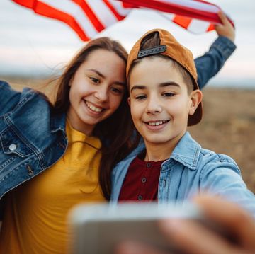 two young teens in field taking selfie with american flag that needs patriotic 4th of july caption