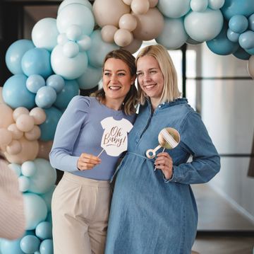 friends pose under a balloon arch as someone takes their photo at a baby shower