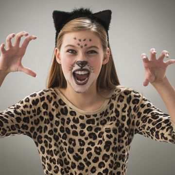 a girl in kitty ears and leopard print shirt has halloween face paint like a cat