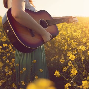 woman holding a guitar in a field of yellow flowers who might be singing easter songs