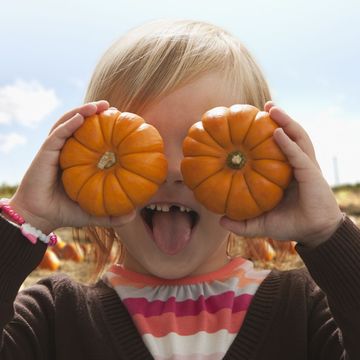 young girl covering eyes with small pumpkins and making a funny face