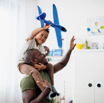 happy little multiracial boy with his father playing together indoors in childrens room