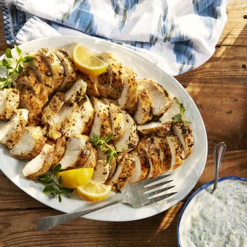 greek chicken on a plate with lemon wedges and tzatziki sauce
