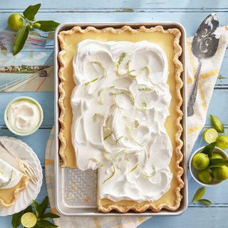 key lime slab pie in a baking tray on a blue table with whipped cream and candied lime on top