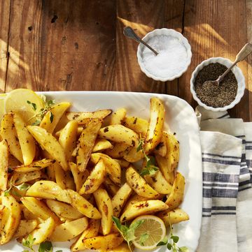 greek style roasted lemon potatoes on a serving dish with sprigs of oregano and sliced lemons