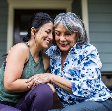 mother and adult daughter who clearly share unbreakable bond, laughing, hugging on porch