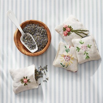 four small linen sachets embroidered with flower designs beside a bowl of dried lavender and a scoop