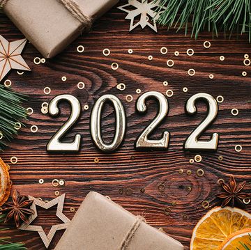 new year 2022 greeting card number 2022  in over dark wooden brown background with confetti, gift boxes, pine, wooden decorations and orange slices