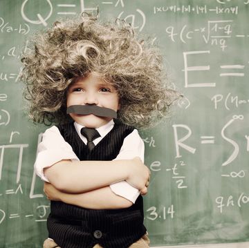 kid dressed like einstein with wig and mustache standing in front of chalkboard covered in equations