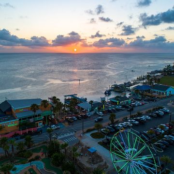 the sun setting over the ocean with restaurants and night life happening on the shore