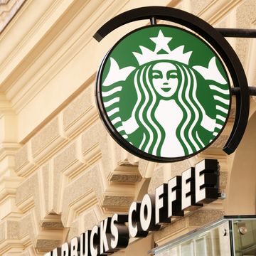 vienna, austria   may 1, 2012 green starbucks coffee logo on a pole and starbucks coffee text on facade of an old house in vienna center diagonally photographed focus on logo  starbucks is known for large to go coffee