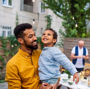 happy young father holding his little son laughing and having fun during family dinner outdoors in back yard